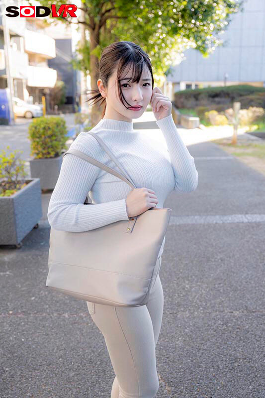 白いリブニット姿の彩月七緒が屋外を歩く場面。バストのシルエットが際立つ追跡視点風のサンプル画像