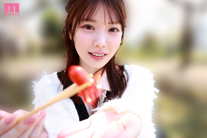 白いファー風カーディガン姿の石川澪が、ハート形のいちごを箸でこちらへ差し出す近距離カット